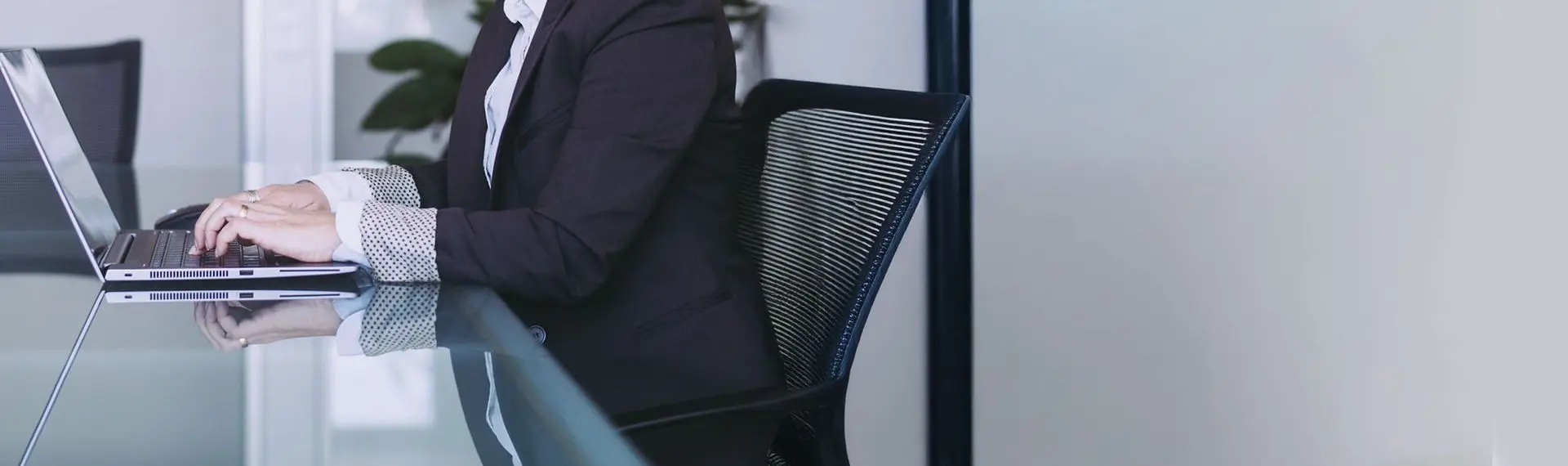 Person im Business-Anzug arbeitet an einem Laptop an einem Glastisch in einem modernen Büro.